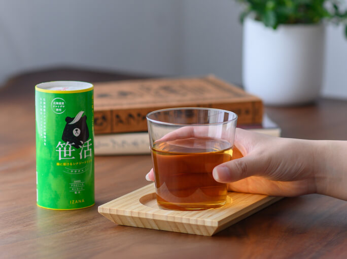 清潔感と温かみのある食卓で笹茶のボトルが置かれていて、ガラスのコップで笹茶を飲んでいる様子。