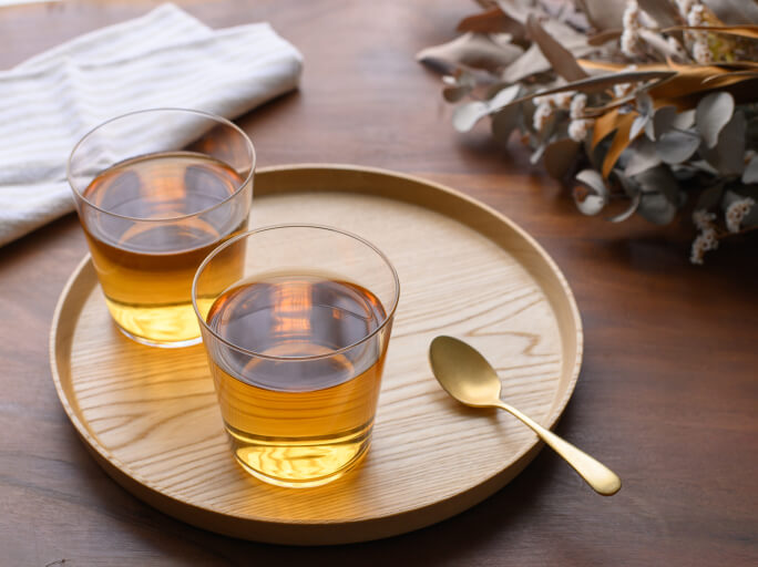 清潔感と温かみのある食卓で、お盆の上に笹茶を注いだガラスのコップが２組ある様子。