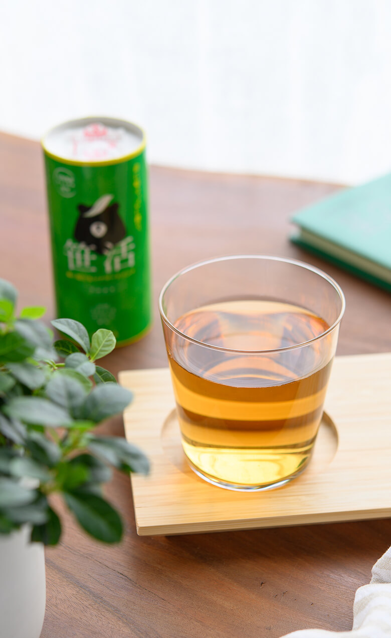 白いカーテンを背景に木目のテーブルがあり、笹茶のボトルと笹茶が注がれたガラスのコップがお盆に置かれている。暖かな日差しが差し込み、全体的に清潔感と親しみやすさが感じられる。